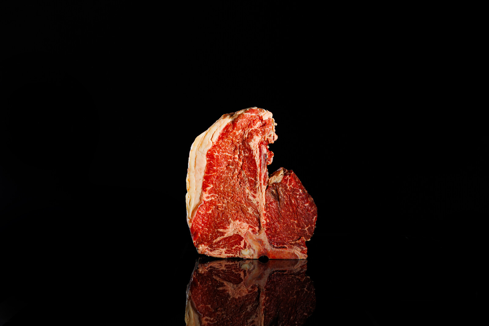 Bistecca spessa con l'osso a T, in piedi su fondo nero lucido