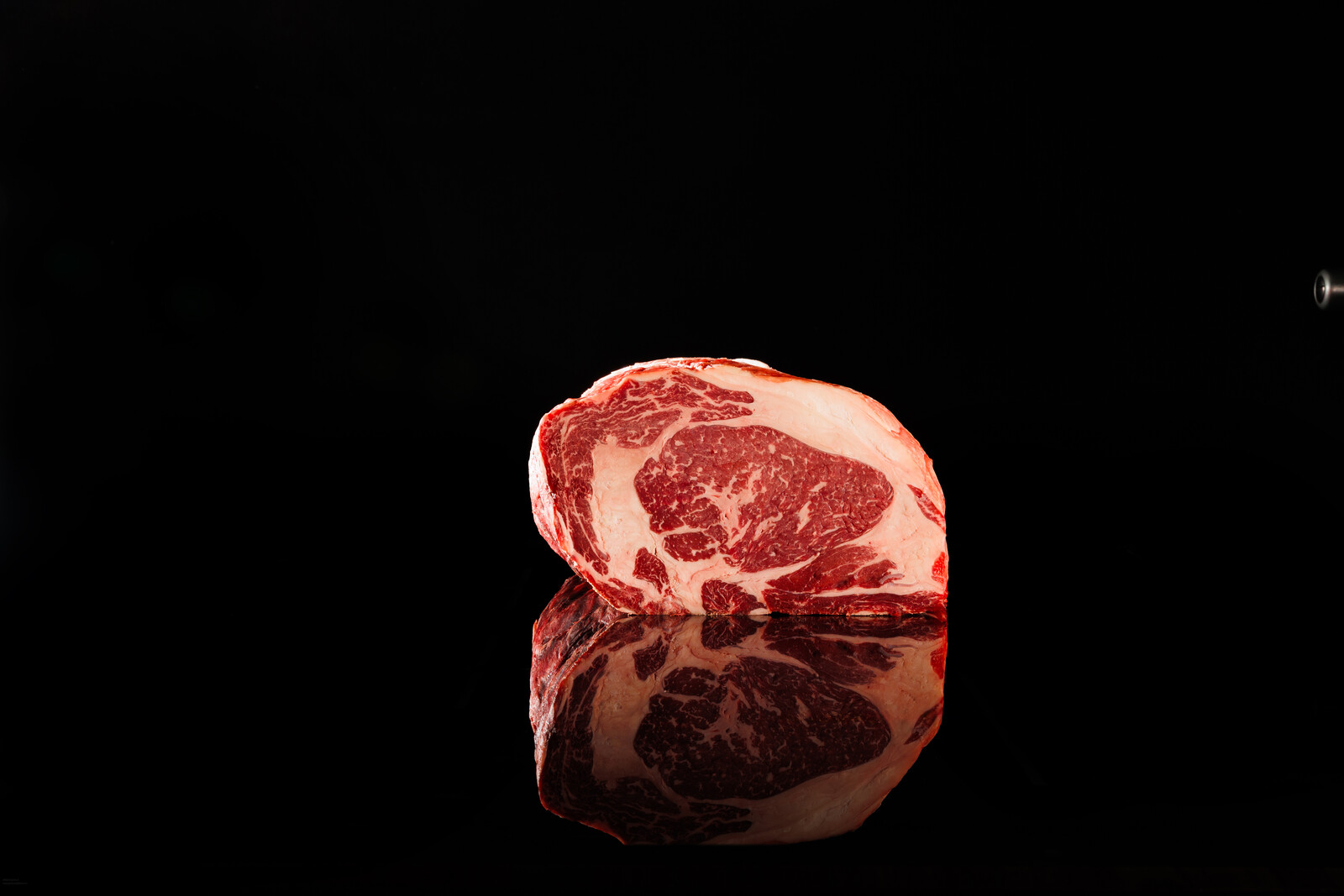 Ribeye crudo senza osso su fondo nero lucido, con la marezzatura in evidenza